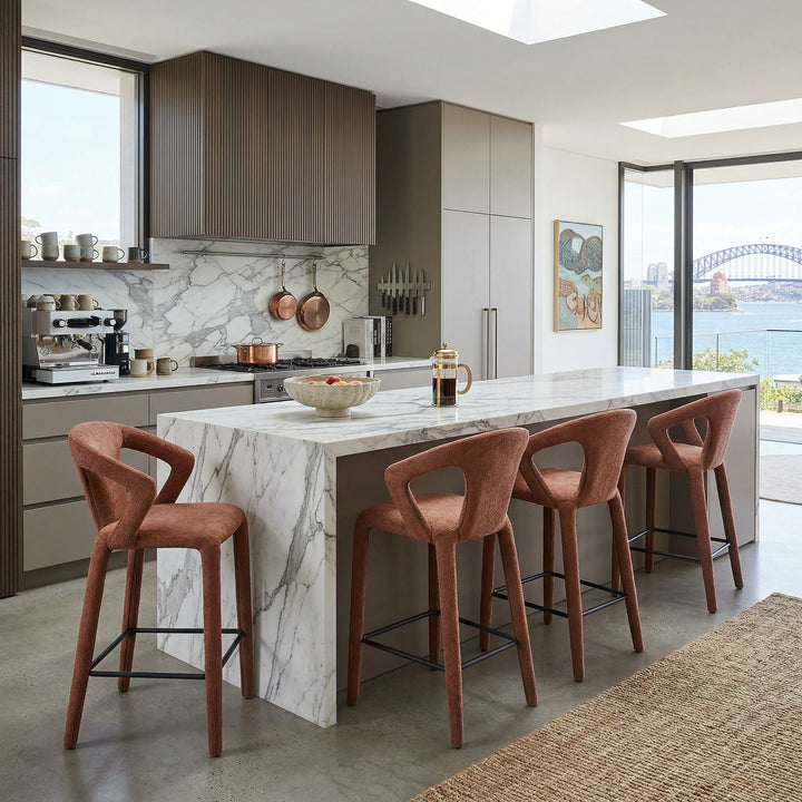 Burnt orange profile bar stool with a sleek modern design, featuring a curved seat and metal base in a contemporary kitchen setting.