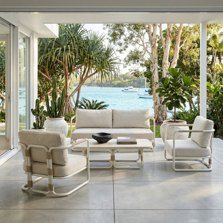 Cream outdoor sofa with plush cushions and sleek design, set on a patio with a travertine coffee table in the background.