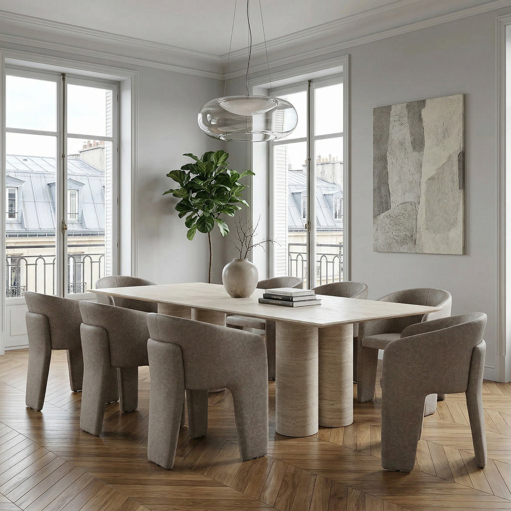 Image of a mushroom leather look Isabella dining chair paired with a travertine dining table in a modern dining room setting.