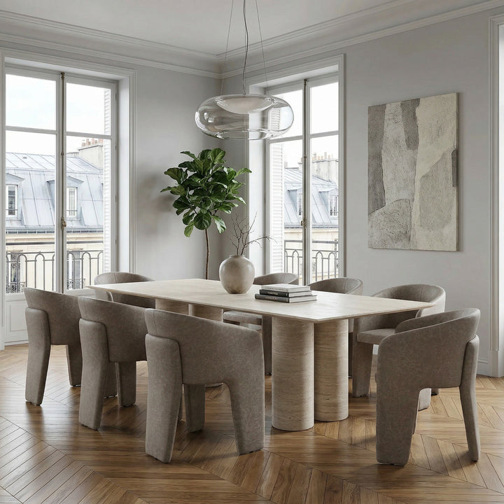 Mushroom leather-look Isabella dining chair with sleek design, shown next to a large travertine dining table in a modern dining room setting.